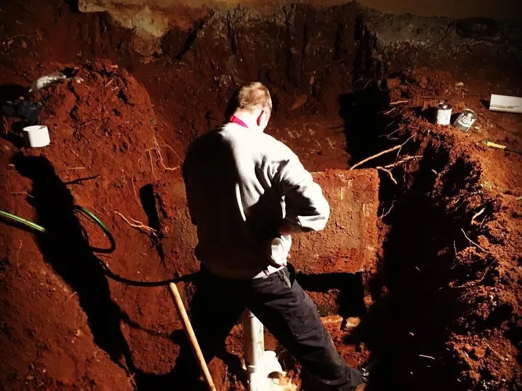 Technician working in a deep excavation to reach a septic tank