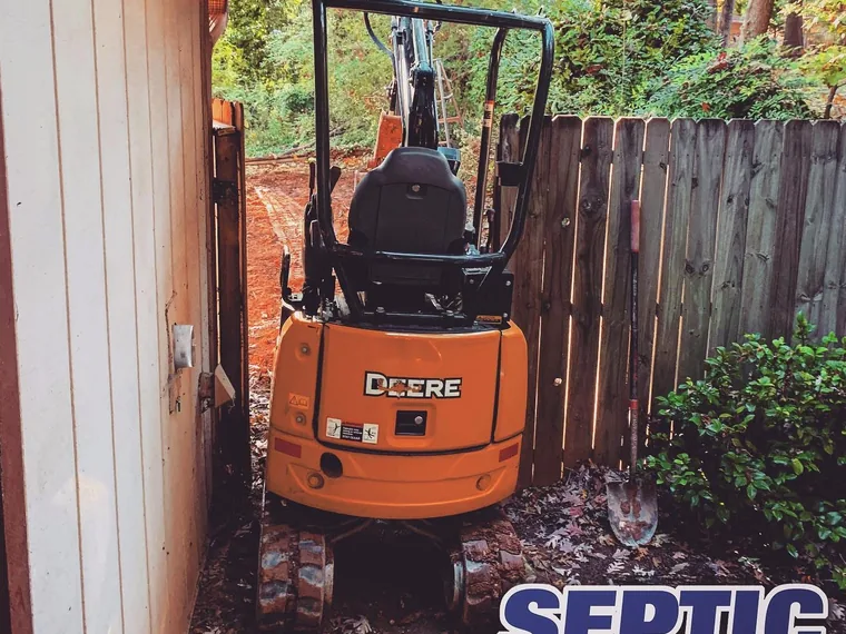John Deere mini-excavator maneuvered into a tight side yard for a repair